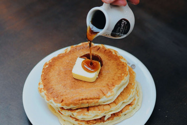 Hand pouring syrup over pancakes; Photo by Pexels, Matheus Gomes
